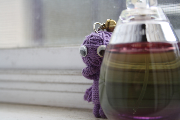 A small crying voodoo doll on a window sill next to a perfume bottle