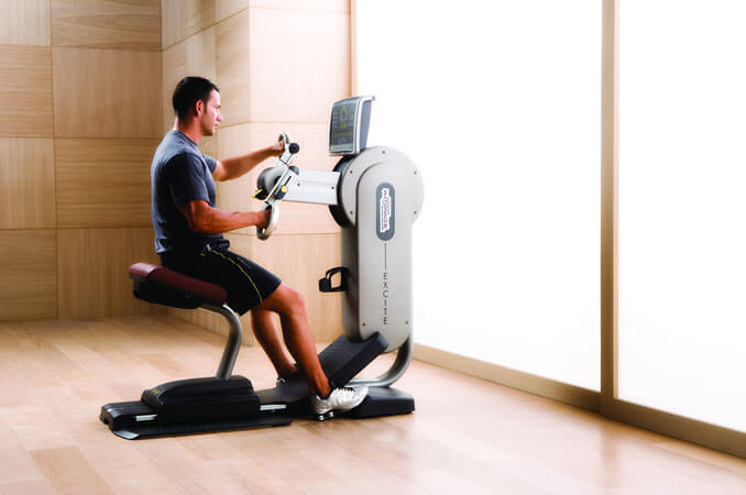 A man sitting on an ergonomic arm cycle machine with his hands in the pedals.