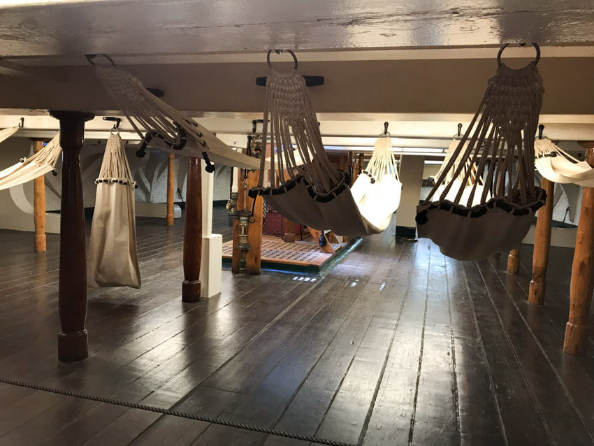 hammocks hanging from the low ceiling of the inside of a ship