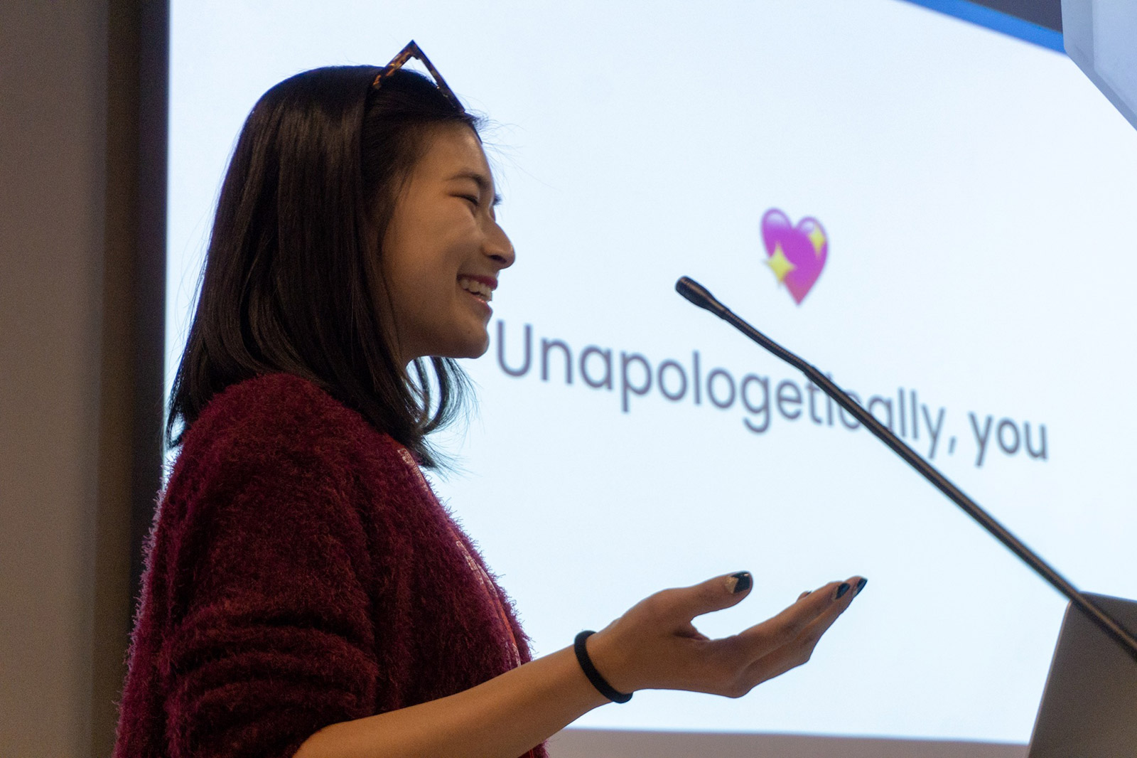 A woman with her palm upturned, in front of a screen reading “Unapologetically, you”