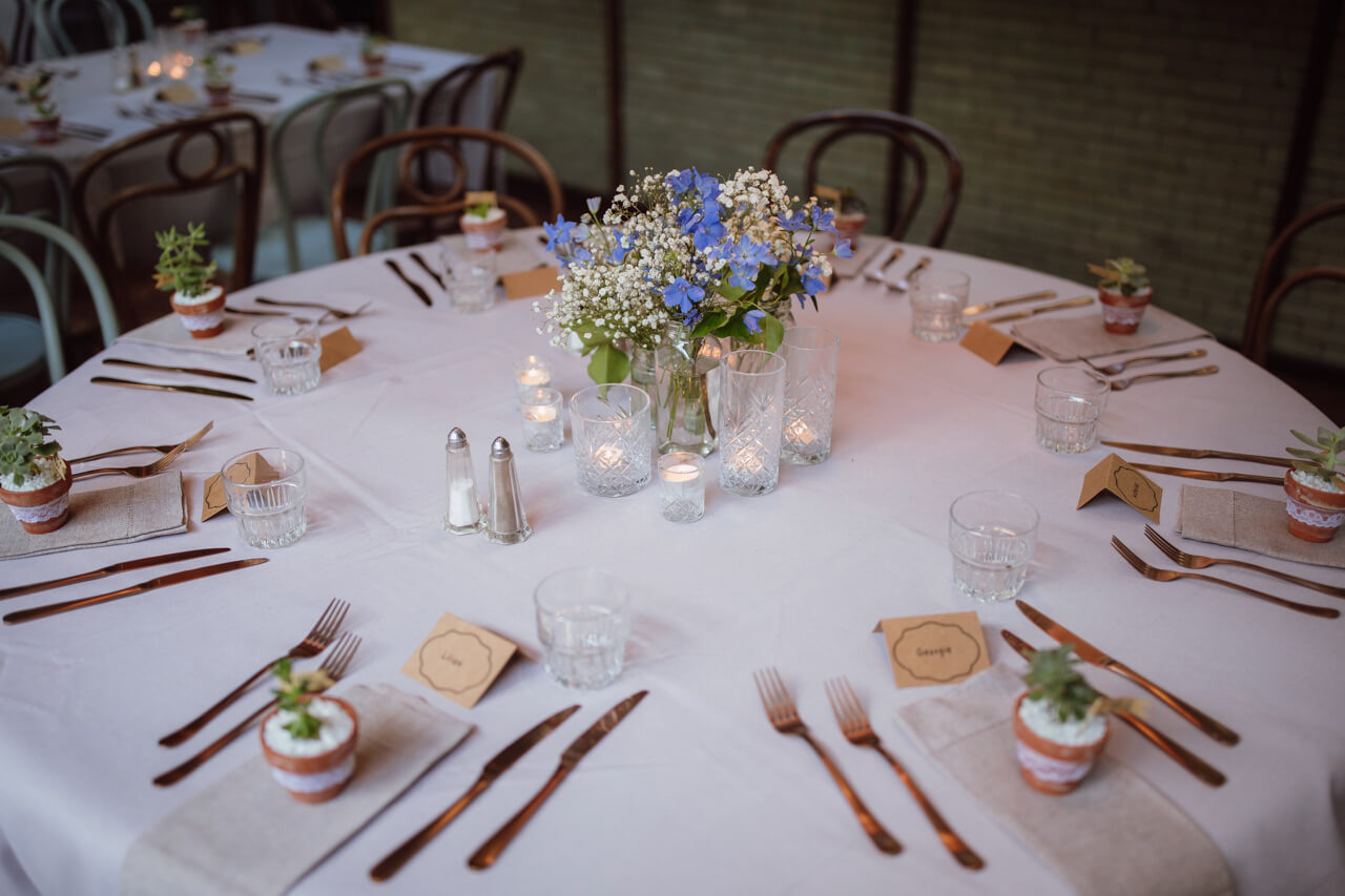 A white round table set up with votives, a floral centrepiece, and cutlery at each seat