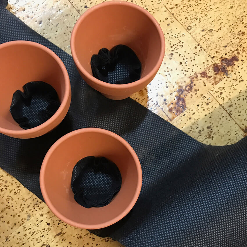 A few small terracotta pots lined with black fabric, sitting on a strip of black mesh fabric