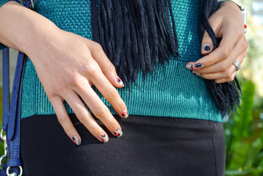 Close up of a woman’s hand with pink, black and light green nail art. She’s wearing a green top and a black skirt.