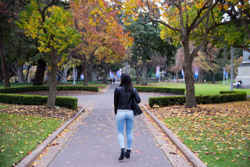 A view from the back of a woman walking down a path with autumn trees in the background.