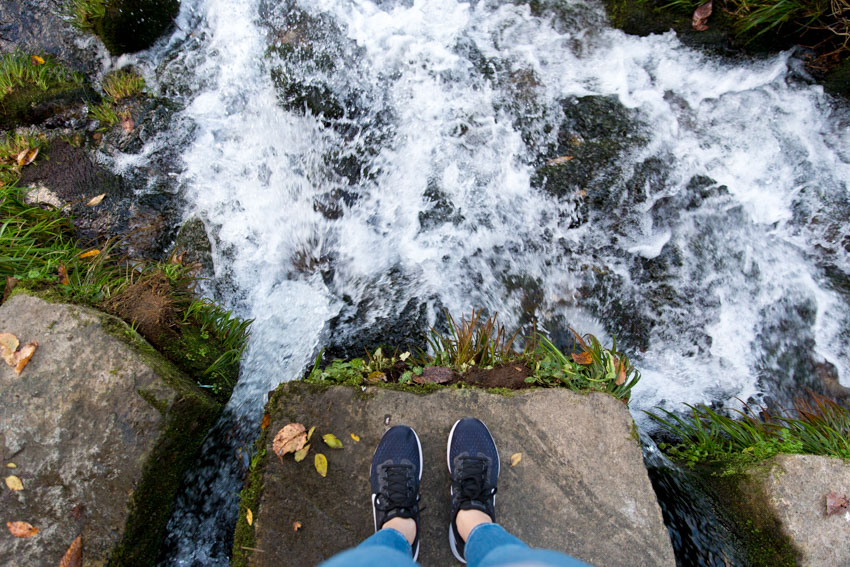 A bird’s-eye view of my Nike shoes with the river splashing on the rocks around me and the rock I am standing on