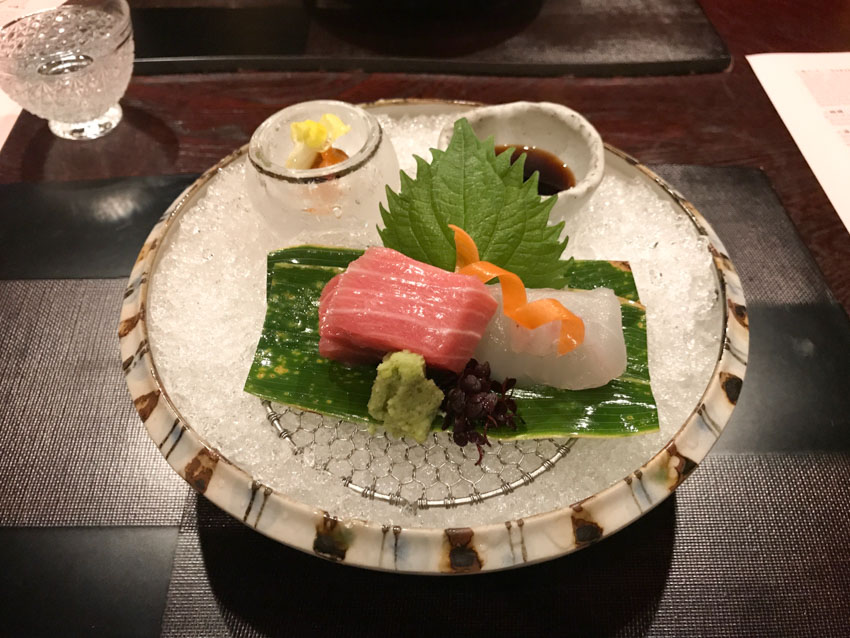 Stone bowl with crushed ice serving as a bed for some raw fish, with a small deep saucer of soy sauce