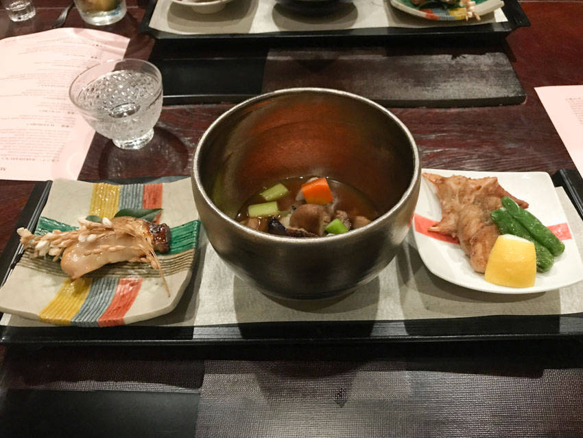 Three dishes: round bowl in the middle with a stew, square plates on left and right with Spanish mackerel and globe fish with green pepper, respectively
