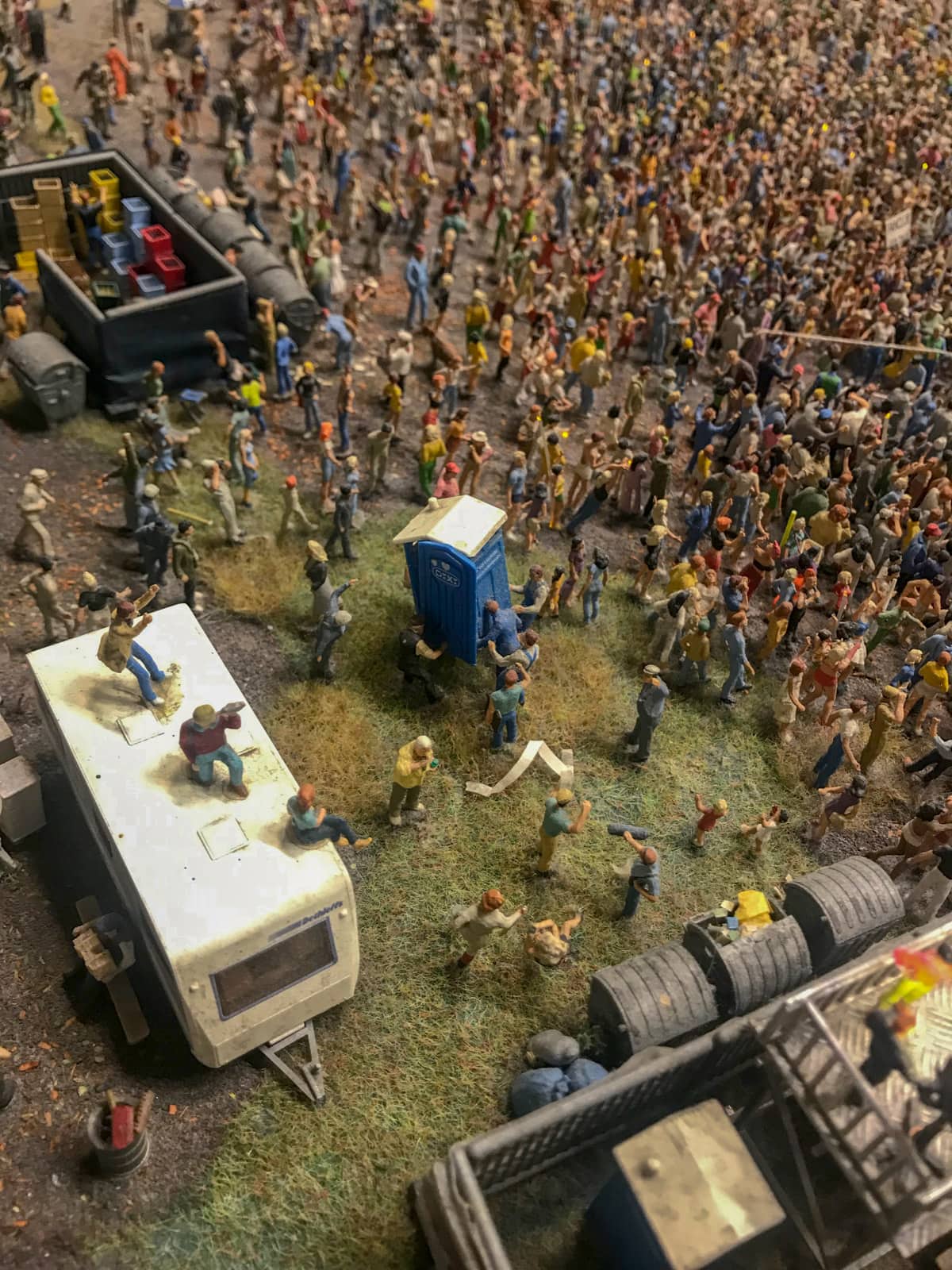 Miniature figurines assembled in a crowd like a festival crowd. There are some figurines carrying a portable toilet