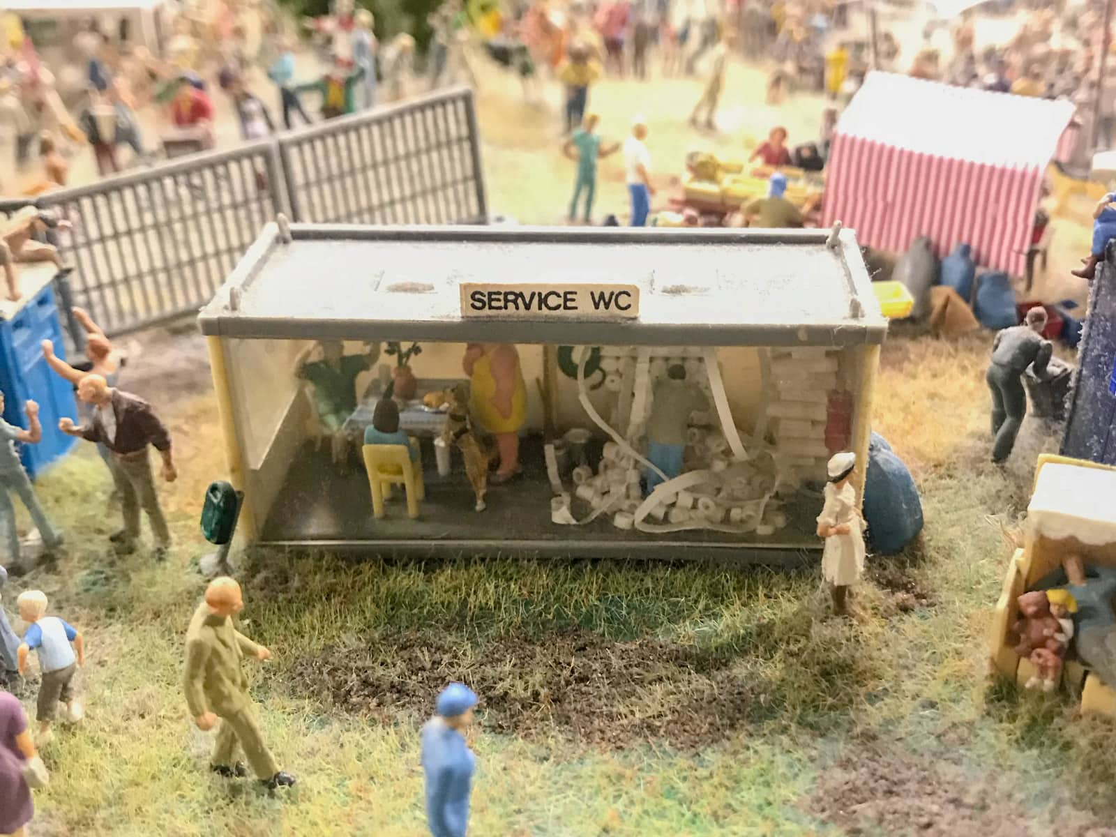 Miniature figurines inside a glass-walled block called “Service WC”. There is a figurine man who seems to be dealing with a shelf of toilet paper