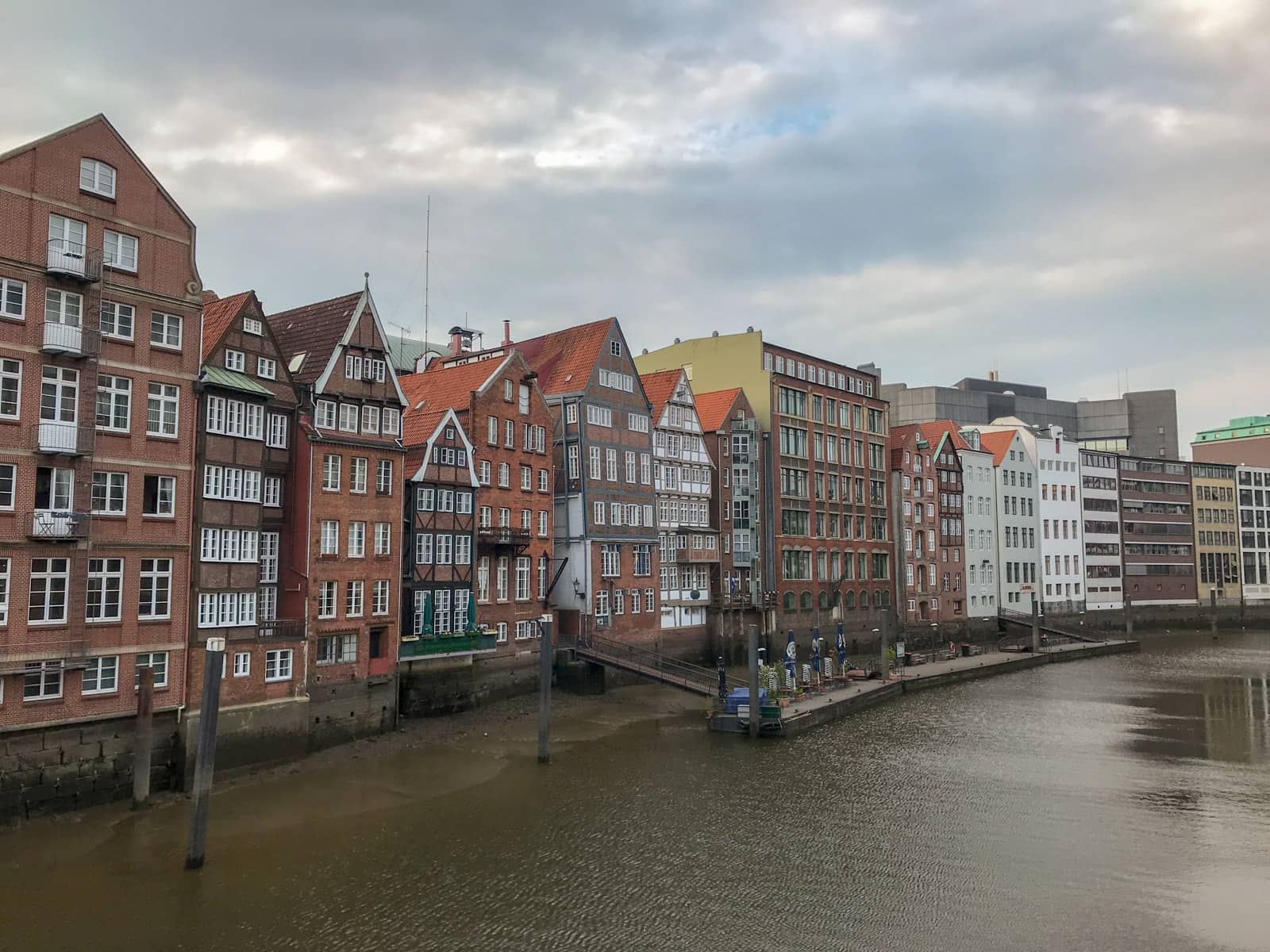 Some large, multi-storey terrace-like houses on the bank of a river, as seen from a distance across the river. It is quite a cloudy day.
