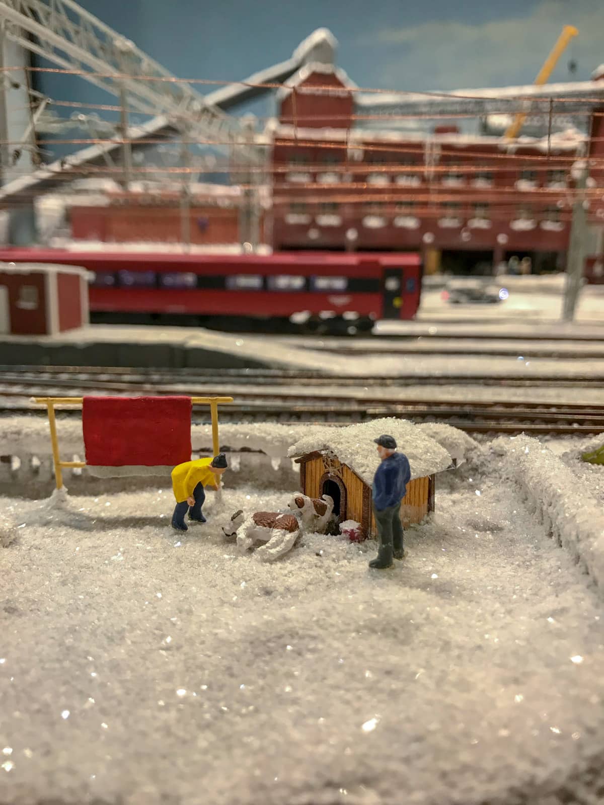 Miniature figurines in a scenario where a man is bending over looking at a dog lying in the snow