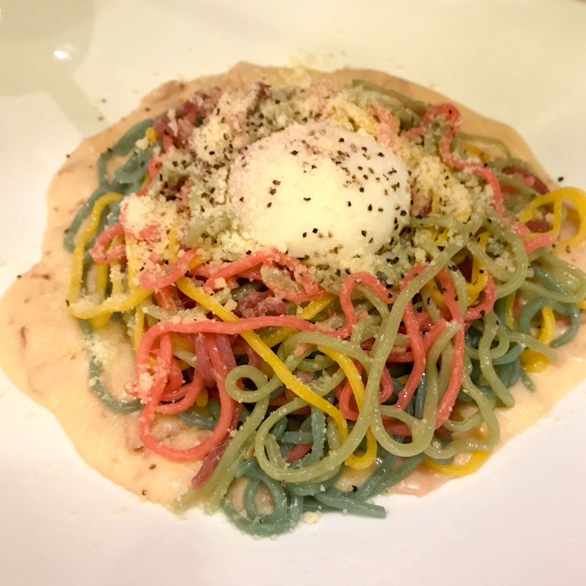 Colourful spaghetti with grated cheese and white pasta sauce on a white plate