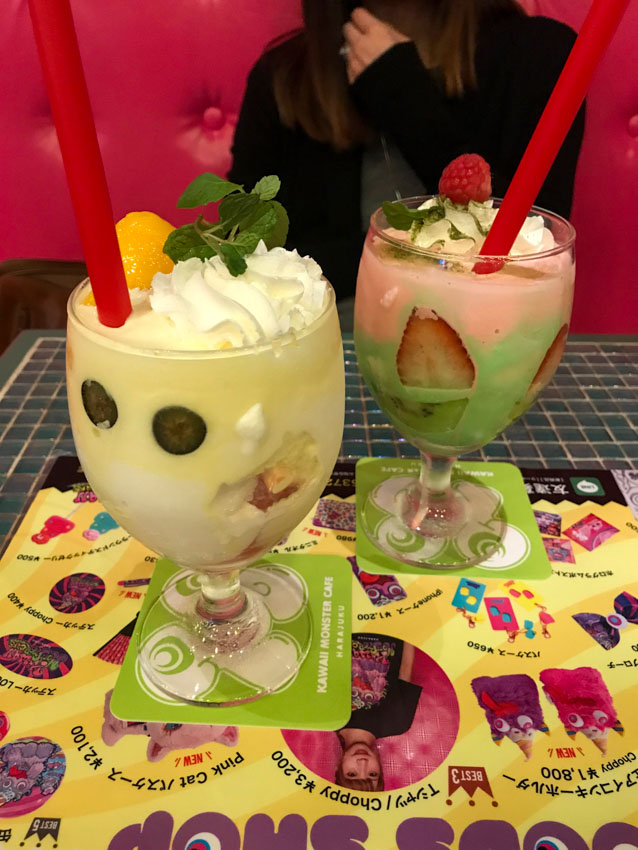 Two wine-shaped glasses, filled with fruit and cream, on square cardboard coasters