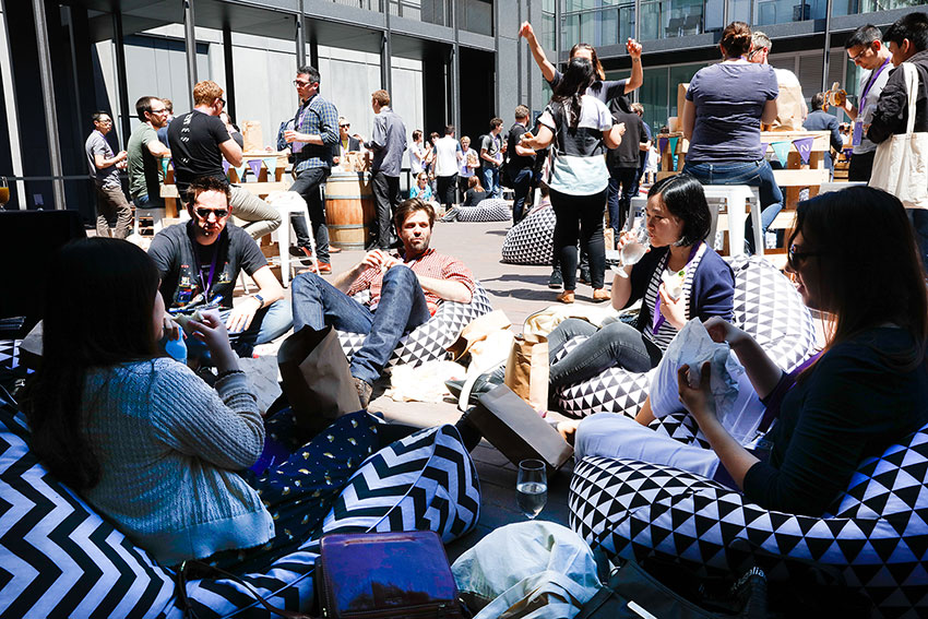 People sitting on black-and-white patterned beanbags, eating and drinking. Many people in the background conversing and eating as well.