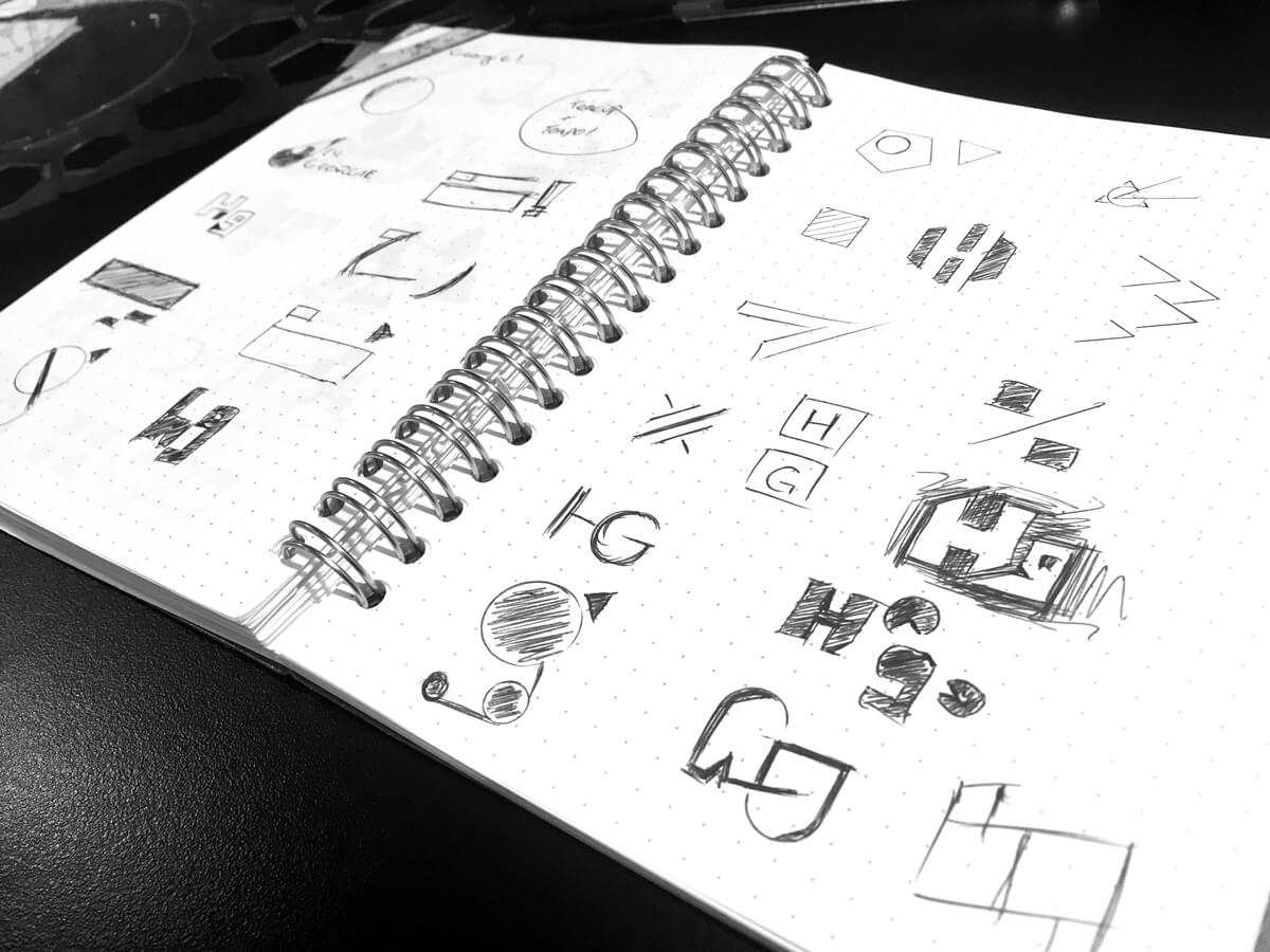 A dot grid spiral bound notebook with various logo sketches