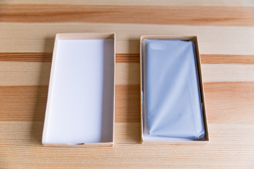 An open brown box and its lid, side by side. In the brown box is a phone case in transcluent plastic.