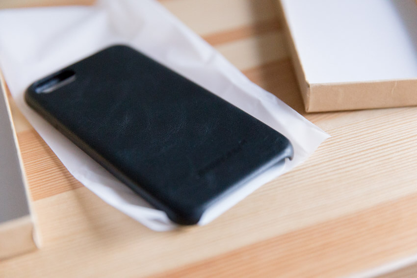 A black leather phone case, its back visible, on a piece of translucent plastic