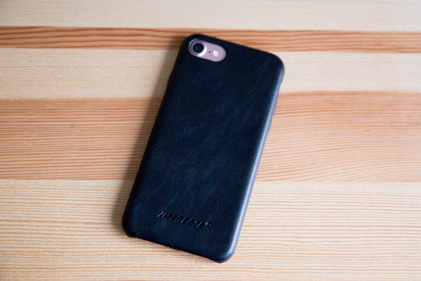 An iPhone with a black leather case, screen-down on a wooden surface