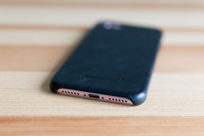 A view of the base of a pink iPhone with a black case with the speaker holes and charging port visible