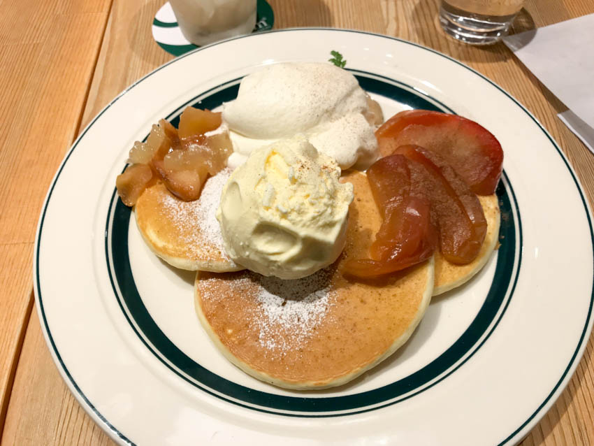 Plate is sweet pancakes with peach/apple and whipped cream