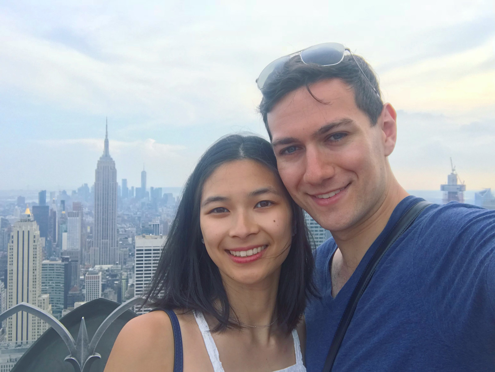 A selfie of a man and woman, smiling. The buildings of New York City are in the background.