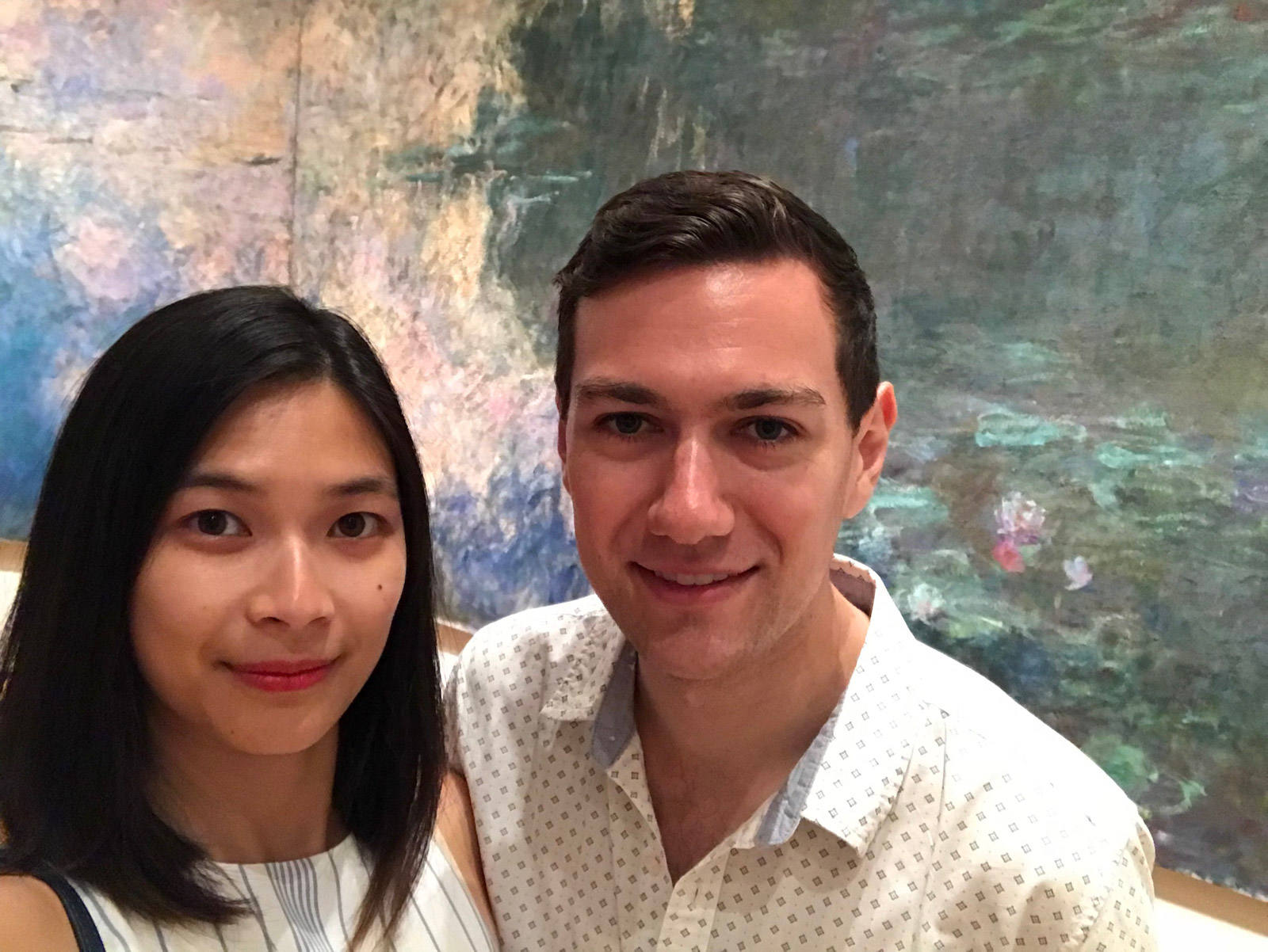 A man and woman, smiling, with a mural painting of water lilies behind them
