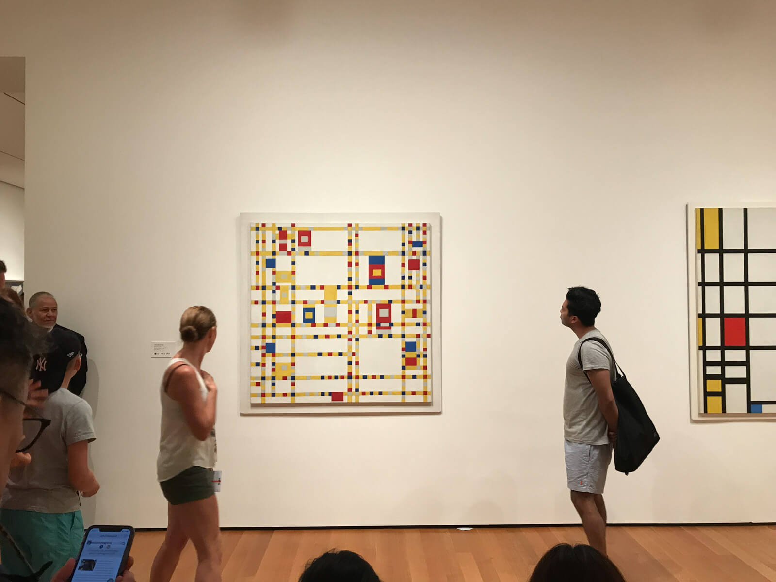 The inside of an art gallery with a geometric-style artwork of a Mondrian grid on the wall. Some people can be seen looking at it from the sides