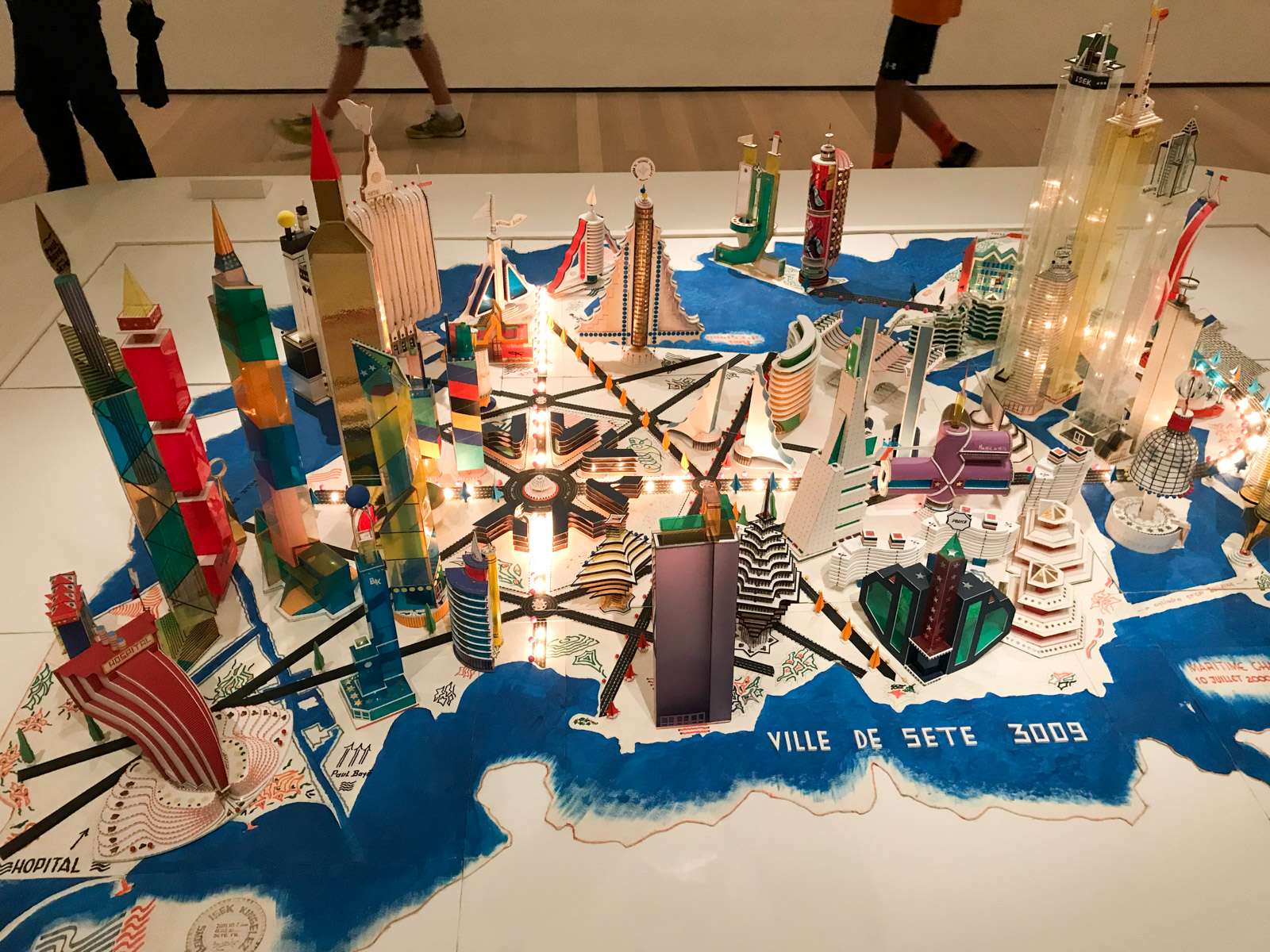 A high angle view of a sculpture made out of mostly coloured cardboard, assembled together like a city on an island