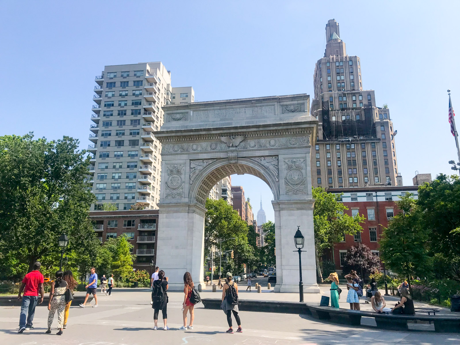 The Washington Square Park arch during the daytime. In the distance, the tall Empire State building can be seen through the arch.
