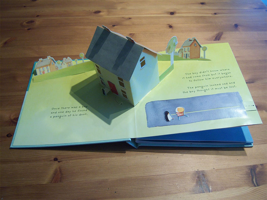 A pop-up book open to a page with a pop-up house in the middle