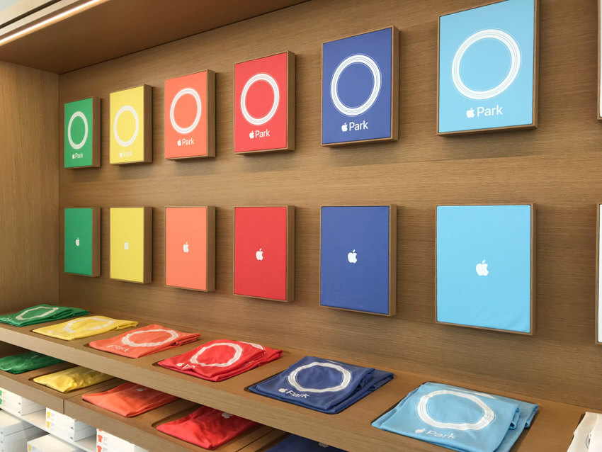 A display of the designs of six different coloured shirts on a wooden background, all reading “Apple Park” with an Apple logo in place of the word “Apple”