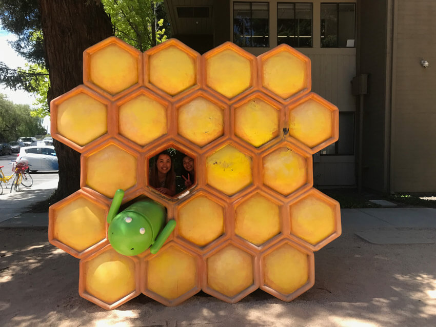 A sculpture resembling a honeycomb, with the Google Android robot in one honeycomb hexagon, and one hexagon free. Two women are looking through the free hexagon from behind and smiling
