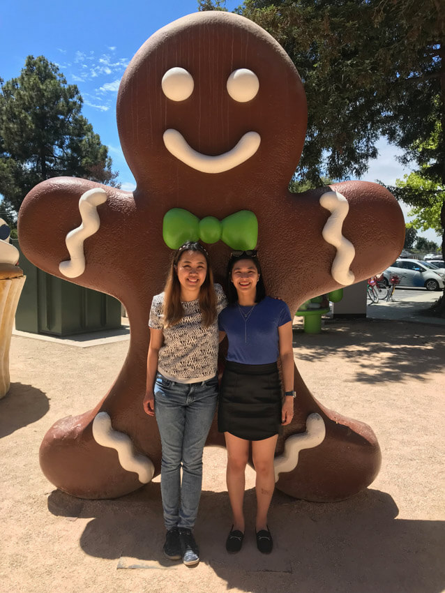 Two women smiling, with their arms around each other, and a giant brown gingerbread statue behind them