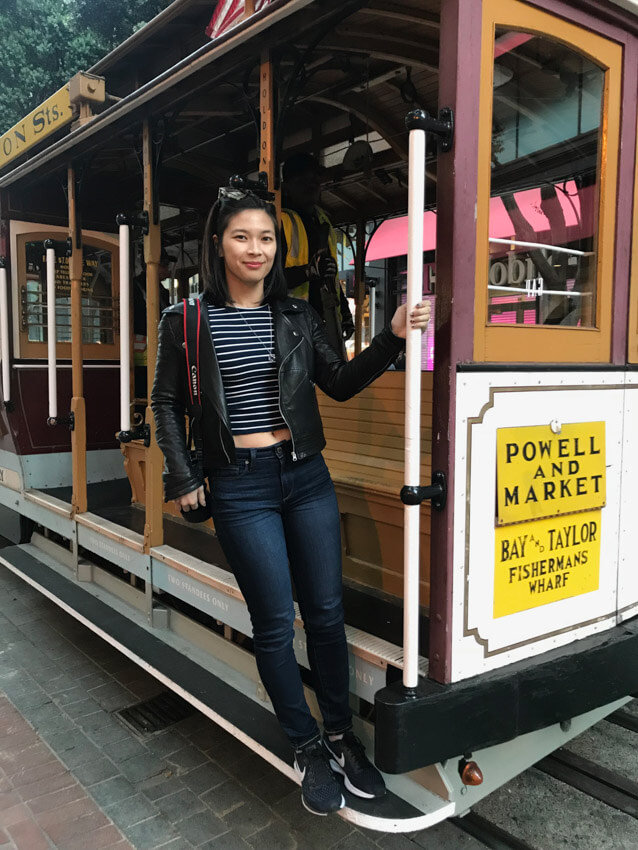 A woman in dark jeans and a striped top and leather jacket, holding onto the side of a cable car