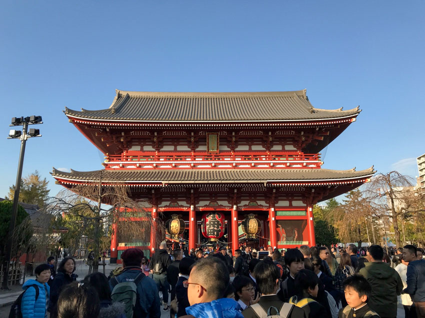 A Japanese temple with crowds of people in front of it, on a day when the sky is clear.