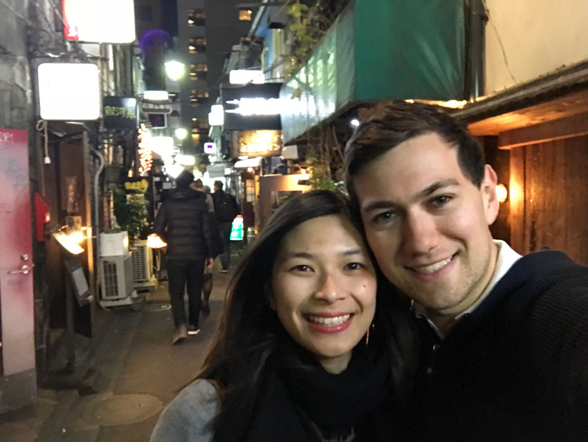 A selfie of me and Nick, both smiling, with neon signs in the background above the bar and eatery entrances in a Golden Gai alleyway