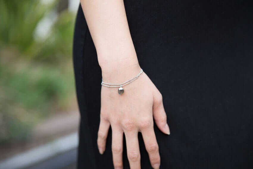 Close shot of a woman’s wrist wearing a silver bracelet with two chains. From one chain hangs a labradorite pendant.