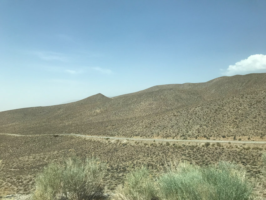 A slightly mountainous desert-like area with a thin road stretching from left to right.