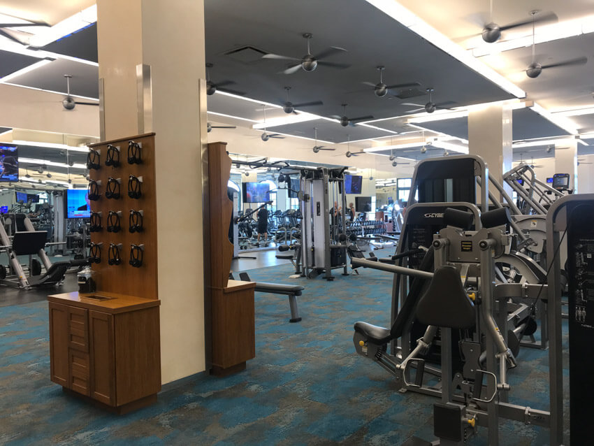 An indoor gymnasium with several machines. In the foreground is a wooden rack with headphones hanging from it.