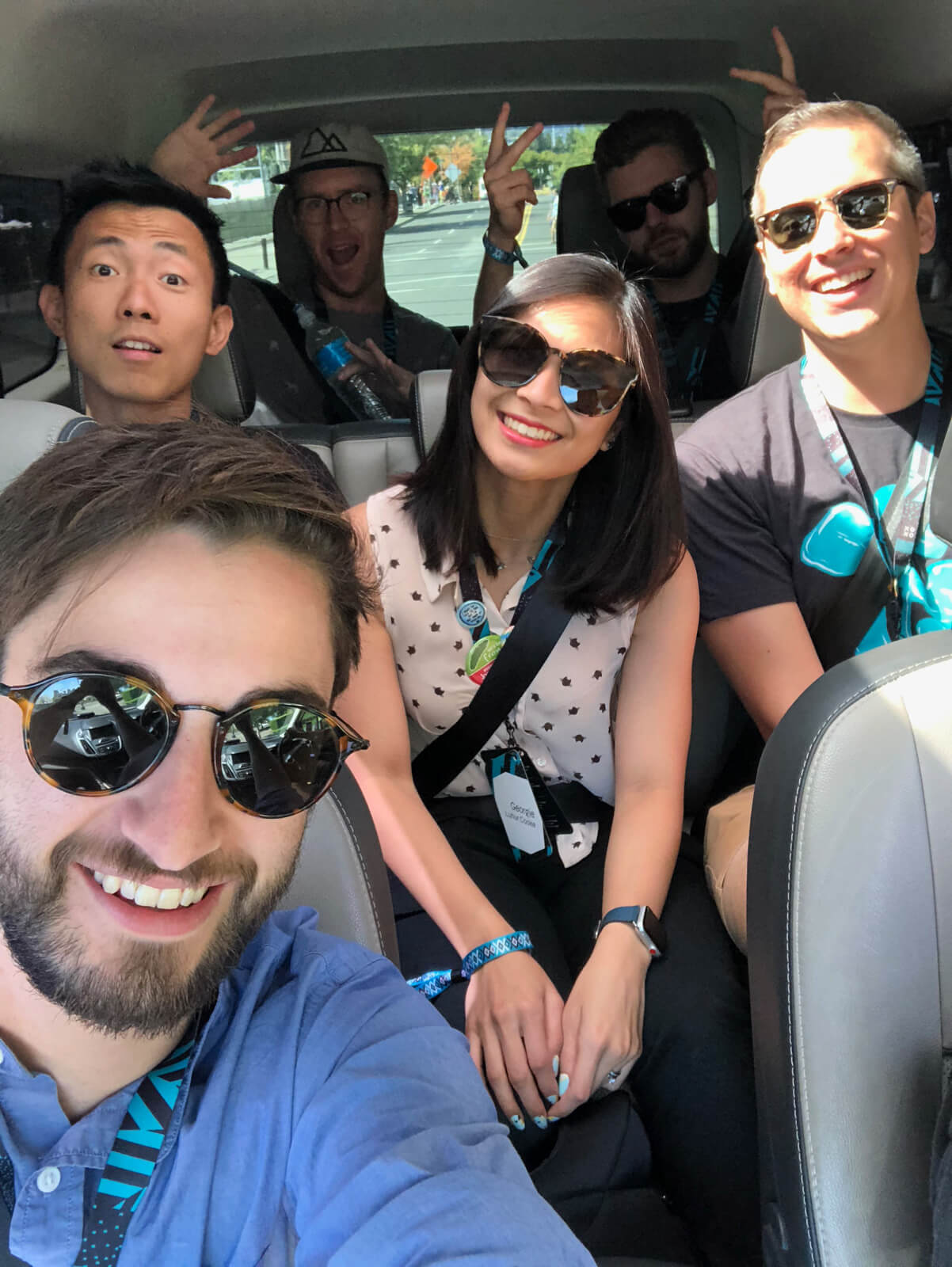 A selfie taken in a car, taken by the man in the passenger seat. There are three people in the second row and two people in the back of the car