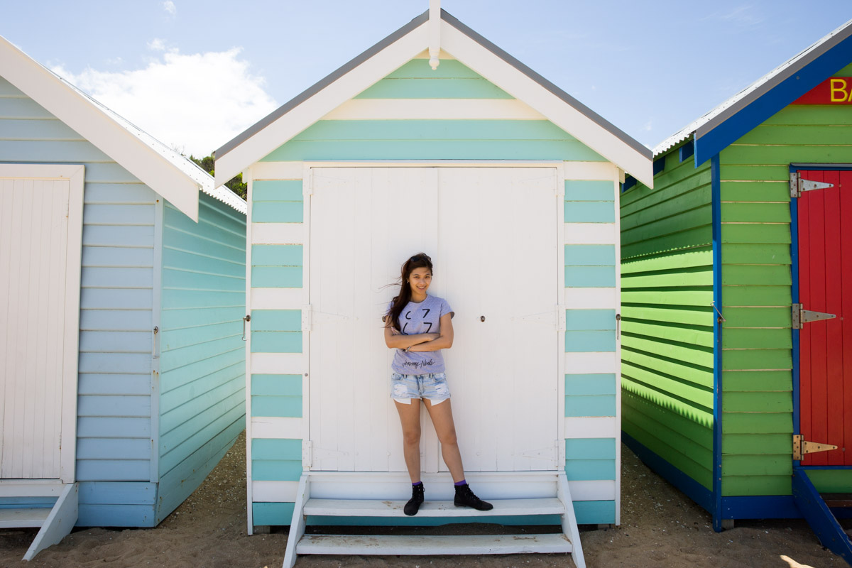 Me standing in front of one of a pale blue and white striped beach hut.