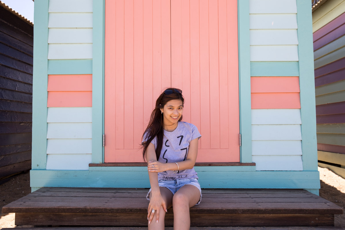Me sitting in front of a pastel blue and peach-pink hut