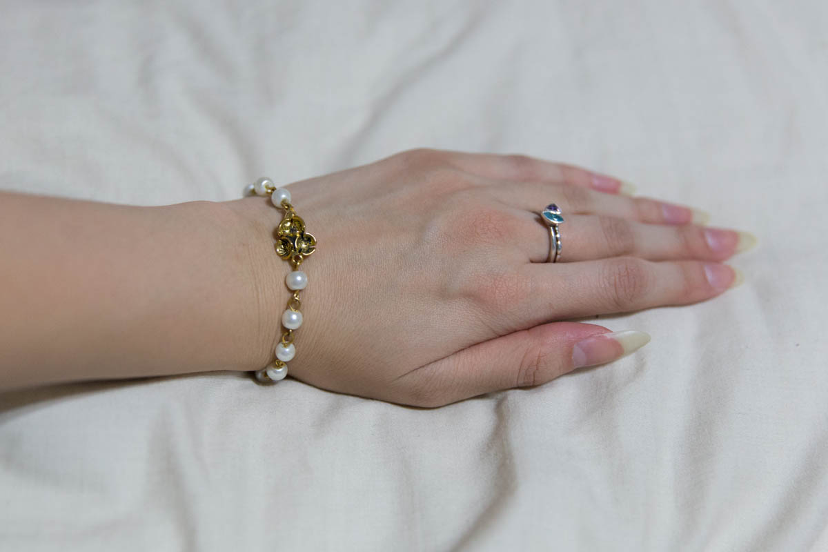 The gold bracelet with white beads on my wrist 