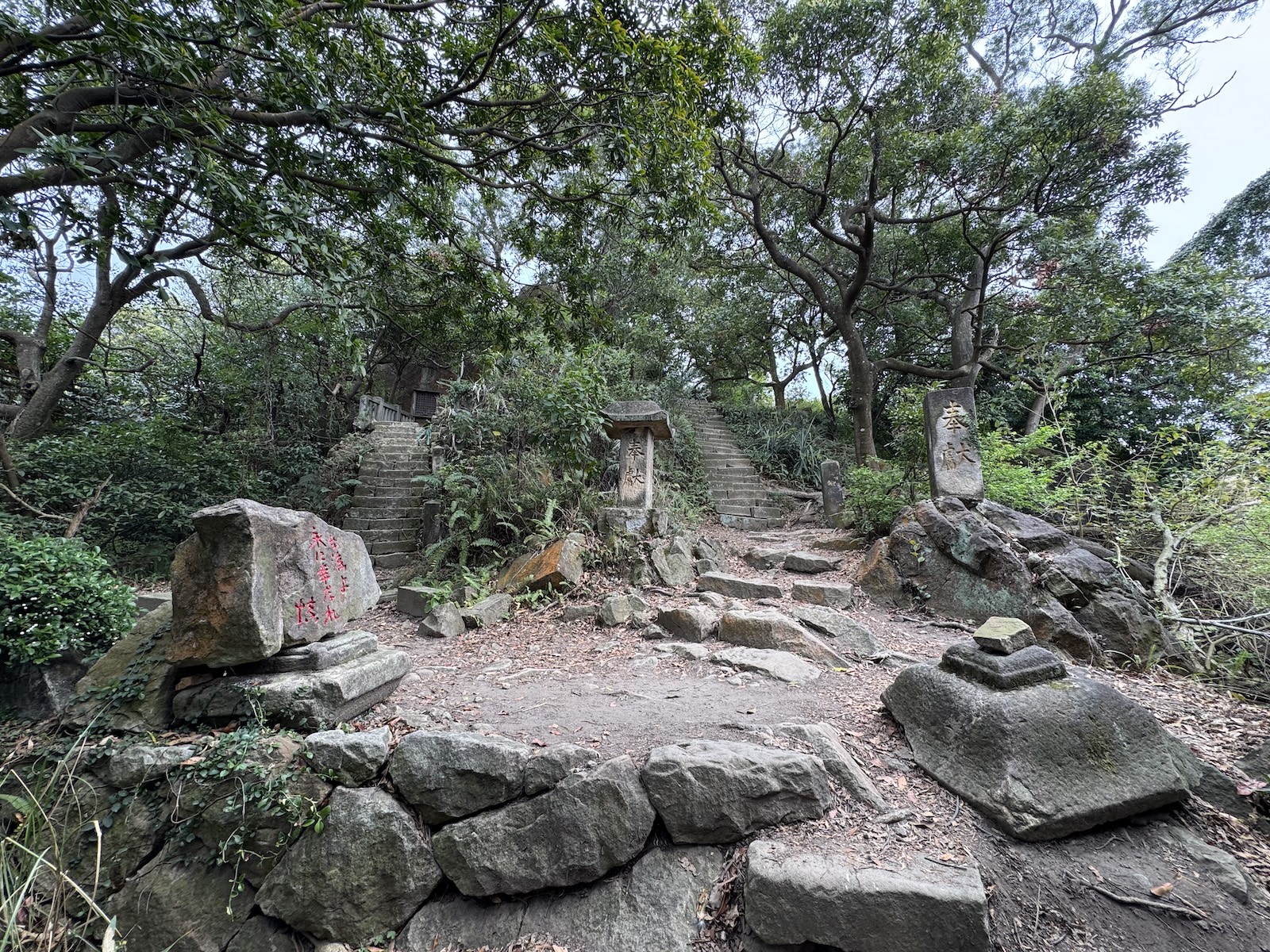 Stone steps lead through a wooded clearing at the Danfeng Mountain historic shrine area. Weathered stone markers and a small stone lantern base sit among the rocks and fallen leaves.