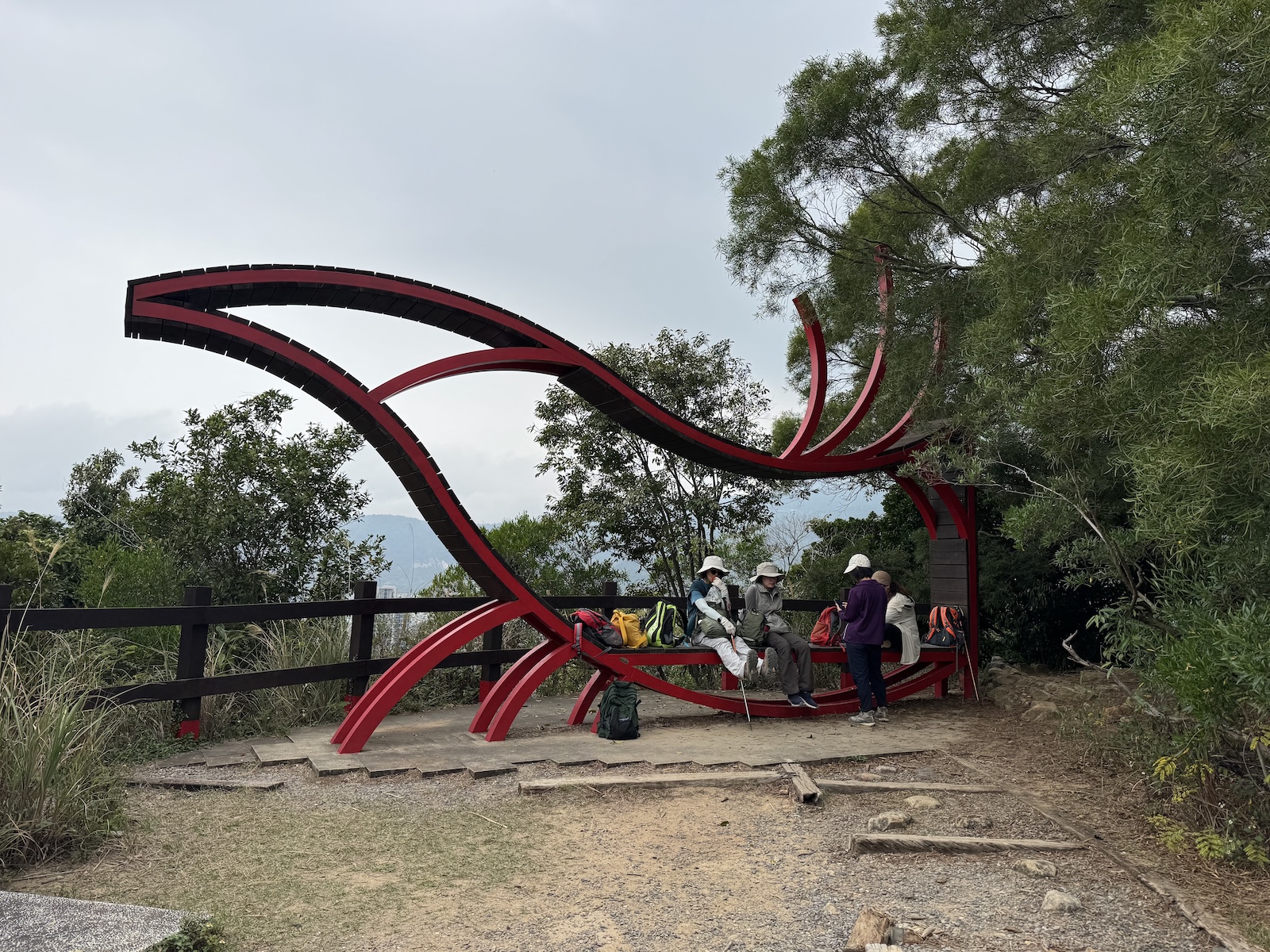 Hikers gather beneath a large red, phoenix-shaped sculpture at the Danfeng Mountain summit lookout in Beitou. The open platform is bordered by trees and a dark wooden railing