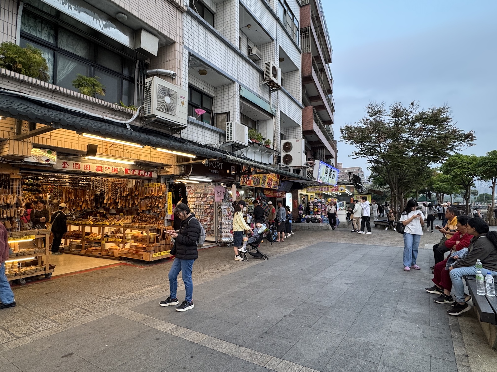 Visitors stroll past brightly lit shops on Tamsui Old Street, a busy waterfront area known for food stalls and souvenir shopping
