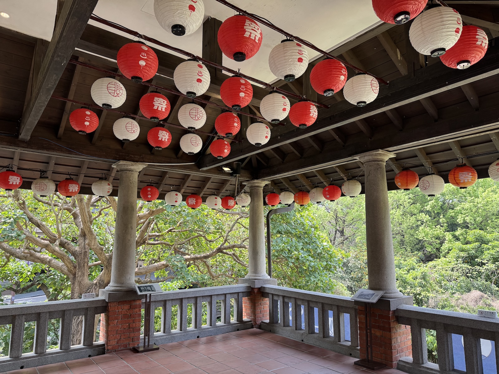 Red and white lanterns hang beneath the timber roof of a covered balcony, overlooking a Park. The museum occupies the restored 1913 public bathhouse.