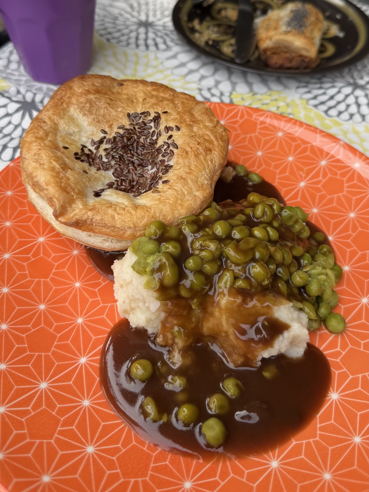 A pie paired with mashed potato and green peas with gravy, served on an orange plate with a light geometric pattern