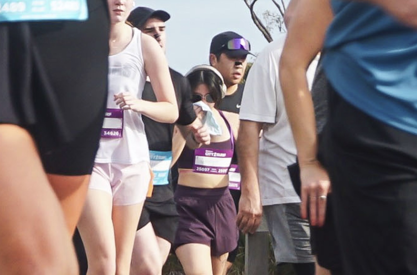 A zoomed-in slightly blurry shot of a running group in athletic gear, with a person in the middle towards the back wearing dark purple gear and holding a handkerchief to their nose