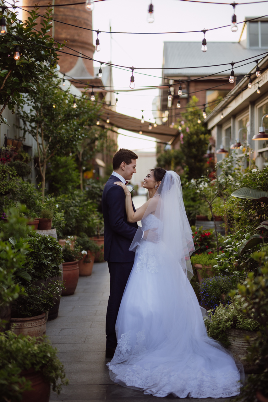 Side view of a bride and groom embracing and looking at each other. They are in a garden setting